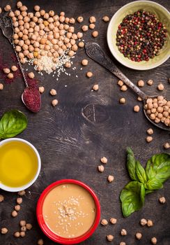 Hummus ingredients. Chickpea, tahini, olive oil, sesame seeds, sumac, herbs on dark rustic wooden background. Space for text. Set of ingredients for making hummus. Middle eastern cuisine. Top view