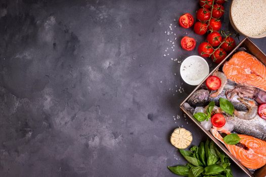 Assorted fish and seafood. Raw fresh salmon steak, trout, squid, shrimps with vegetables and rice ready to cook. Ingredients for cooking on concrete background. Space for text. Diet and healthy food