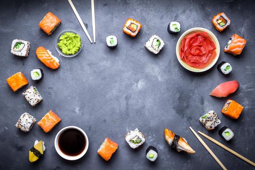 Japanese sushi on a rustic dark background. Sushi rolls, nigiri, maki, pickled ginger, wasabi, soy sauce. Sushi set on a table. Space for text. Top view. Sushi background. Asian or Japanese food frame