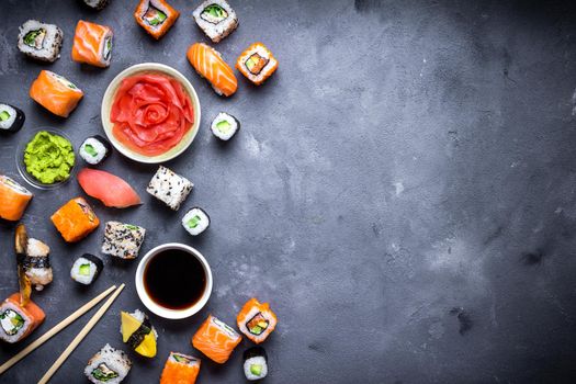 Japanese sushi on a rustic dark background. Sushi rolls, nigiri, maki, pickled ginger, wasabi, soy sauce. Sushi set on a table. Space for text. Top view. Sushi background. Asian or Japanese food frame