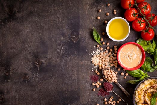 Hummus ingredients. Chickpea, tahini, olive oil, sesame seeds, sumac, herbs on dark rustic wooden background. Space for text. Set of ingredients for making hummus. Middle eastern cuisine. Top view