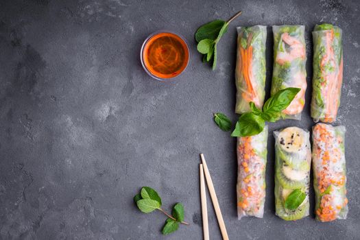 Fresh assorted spring rolls set background. Handmade asian/Chinese spring rolls, sauce, chopsticks. Rustic concrete background. Spring rolls with shrimps, vegetables, fruits. Space for text. Top view