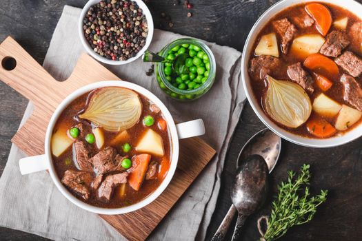 Meat stew with beef, potato, carrot, pepper, spices, green peas. Slow cooked meat stew, bowl, wooden background. Hot autumn/winter dish. Closeup. Top view. Comfort food. Homemade soup/ragout/casserole