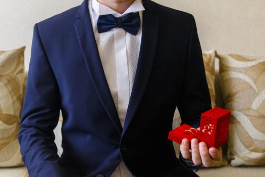 Man in the blue suit holds little gift-box with wedding rings