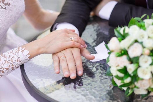 Close-up of wedding hands with rings and bouquet lie on the table