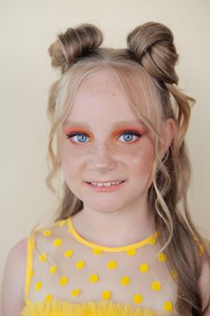 charming blonde tween girl with orange makeup on yellow background. teenager portrait.