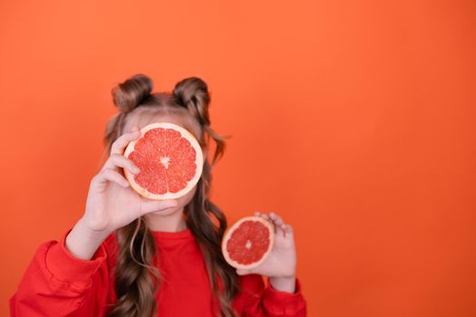 pretty tween girl in orange with a grapefruit isolated on orange background. tropical citrus fruit Grapefruit slices. orange stylish make up. teenager portrait.