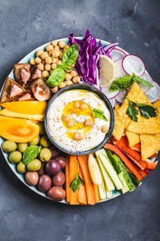 Hummus platter with assorted snacks. Hummus in bowl, vegetables sticks, chickpeas, olives, pita chips. Plate with Middle Eastern/Mediterranean meze. Party/finger food. Top view. Vegetables, hummus dip