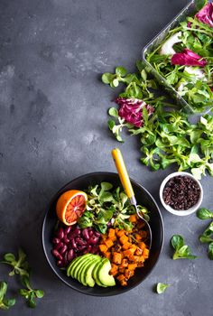 Quinoa salad in bowl with avocado, sweet potato, beans, herbs, orange on concrete rustic background. Quinoa superfood concept. Clean healthy detox eating. Vegan/vegetarian food. Making healthy salad