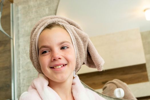 Relaxed young girl model wears towel wrapped on head, feels refreshed after taking shower, has healthy clean soft skin, poses in cozy bathroom. Girl, beauty and hygiene concept. High quality photo