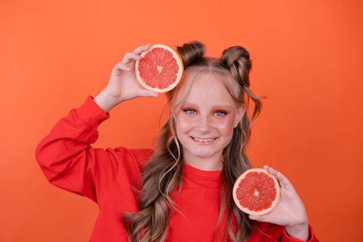 pretty tween girl in orange with a grapefruit isolated on orange background. tropical citrus fruit Grapefruit slices. orange stylish make up. teenager portrait.
