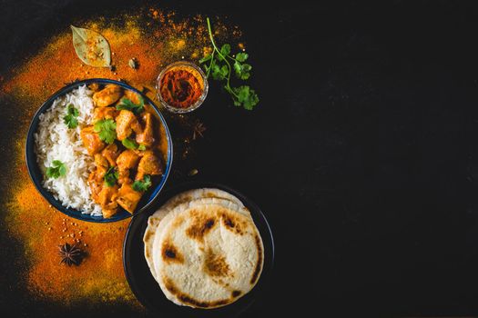 Indian Butter chicken with basmati rice in bowl, spices, naan bread. Black background. Space for text. Butter chicken, traditional Indian dish. Top view. Chicken tikka masala. Indian cuisine