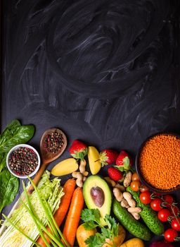 Vegetables, fruits, lentils, raw ingredients for cooking, spoon on rustic black chalk board background. Healthy, clean eating concept. Vegan or gluten free diet. Space for text. Top view. Food frame