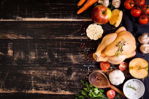 Raw whole chicken ready for cooking. Chicken with vegetables, herbs and spices on a black rustic wooden background. Space for text. Food frame. Diet or healthy eating. Ingredientd for cooking