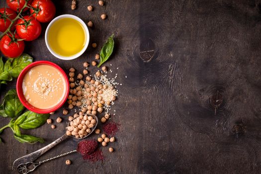 Hummus ingredients. Chickpea, tahini, olive oil, sesame seeds, sumac, herbs on dark rustic wooden background. Space for text. Set of ingredients for making hummus. Middle eastern cuisine. Top view