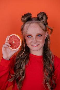 pretty tween girl in orange with a grapefruit isolated on orange background. tropical citrus fruit Grapefruit slices. orange stylish make up. teenager portrait.