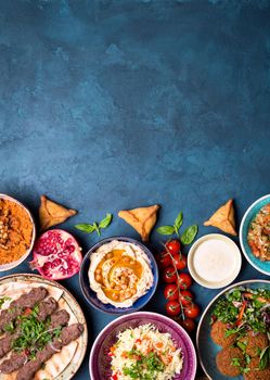 Middle eastern or arabic dishes and assorted meze on concrete rustic background. Meat kebab, falafel, baba ghanoush, hummus, sambusak, rice, tahini, kibbeh, pita. Halal food. Space for text. Top view