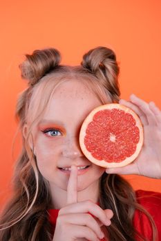 pretty tween girl in orange with a grapefruit isolated on orange background. tropical citrus fruit Grapefruit slices. orange stylish make up. teenager portrait.