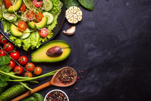 Ingredients for making salad on rustic black chalk board background. Vegetable salad in bowl, avocado, tomato, cucumber, spinach. Healthy, clean eating concept. Vegan or gluten free diet. Copy space