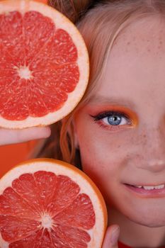 sweet joyful brunette girl female with cropped slice of grapefruit near skin face on orange background. tasty juicy fruit. Tropical citrus fruits, Healthy food. weight loss.