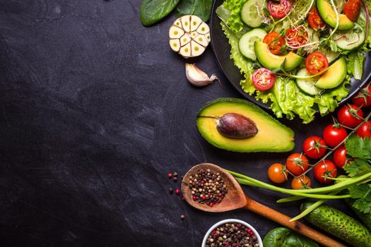 Ingredients for making salad on rustic black chalk board background. Vegetable salad in bowl, avocado, tomato, cucumber, spinach. Healthy, clean eating concept. Vegan or gluten free diet. Copy space