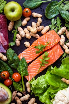 Fresh vegetables, fruits, fish, meat, nuts on black chalk board background. Сauliflower, avocado, apples, tomatoes, salmon, beef, spinach, herbs. Diet/healthy/paleo food. Ingredients for cooking