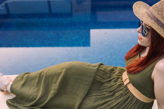 young adventurous girl, sunbathing in front of the pool of her holiday hotel. girl on a pleasure trip. relax and travel concept. Outside, dim sunlight, grass floor with white tiles. copy space.