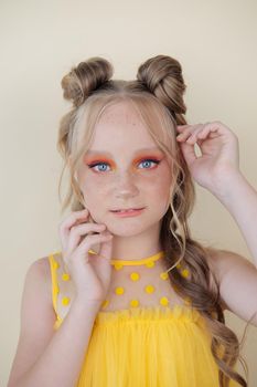 charming blonde tween girl with orange makeup on yellow background. teenager portrait.