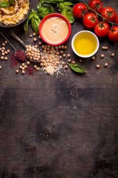 Hummus ingredients. Chickpea, tahini, olive oil, sesame seeds, sumac, herbs on dark rustic wooden background. Space for text. Set of ingredients for making hummus. Middle eastern cuisine. Top view