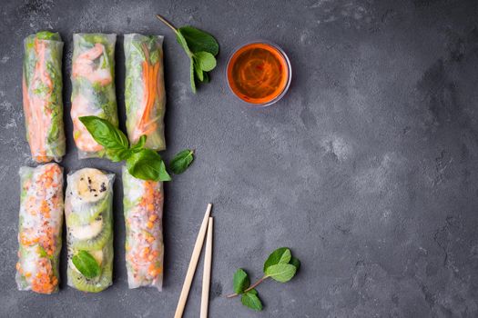 Fresh assorted spring rolls set background. Handmade asian/Chinese spring rolls, sauce, chopsticks. Rustic concrete background. Spring rolls with shrimps, vegetables, fruits. Space for text. Top view