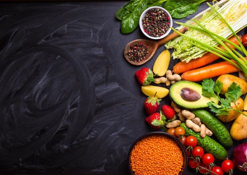 Vegetables, fruits, lentils, raw ingredients for cooking, spoon on rustic black chalk board background. Healthy, clean eating concept. Vegan or gluten free diet. Space for text. Top view. Food frame