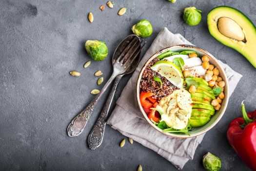 Bowl with healthy salad on grey concrete background. Space for text. Bowl with mix of chickpea, avocado, chicken, quinoa seeds, red bell pepper, fresh spinach, lemon. Clean healthy eating concept