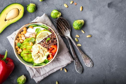 Bowl with healthy salad on grey concrete background. Space for text. Bowl with mix of chickpea, avocado, chicken, quinoa seeds, red bell pepper, fresh spinach, lemon. Clean healthy eating concept