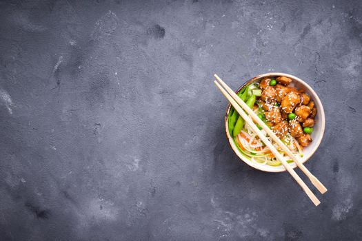 Asian style noodles with teriyaki chicken, vegetables and green peas pods. Noodles in bowl on rustic concrete background. Chinese/thai/japanese style stir fry noodles. Space for text. Top view