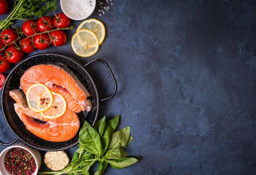 Raw fresh fish with vegetables ready to cook. Raw salmon steak with lemon and spices in a pan. Ingredients for cooking on a concrete background. Space for text. Diet and healthy food. Fish background