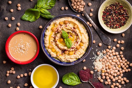 Hummus ingredients. Chickpea, tahini paste, olive oil, sesame seeds, sumac, herbs on dark rustic wooden background. Set of raw ingredients for making hummus. Middle eastern cuisine. Top view