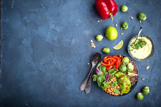 Bowl with healthy salad, dip, blue stone background. Top view. Space for text. Buddha bowl with chickpea, avocado, quinoa seeds, red bell pepper, fresh spinach, brussels sprout, lime. Vegetarian salad