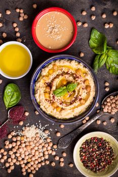 Hummus ingredients. Chickpea, tahini paste, olive oil, sesame seeds, sumac, herbs on dark rustic wooden background. Set of raw ingredients for making hummus. Middle eastern cuisine. Top view