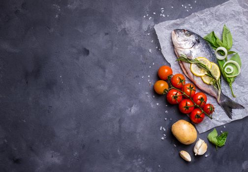 Raw fish with fresh ingredients ready to cook. Fish, lemon, herbs, potato, tomatoes. Ingredients for cooking on dark rustic background. Space for text. Diet and healthy food. Fish background. Top view