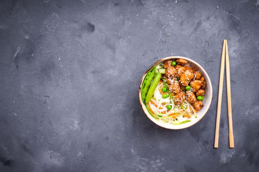 Asian style noodles with teriyaki chicken, vegetables and green peas pods. Noodles in bowl on rustic concrete background. Chinese/thai/japanese style stir fry noodles. Space for text. Top view