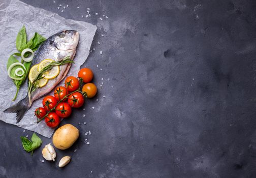 Raw fish with fresh ingredients ready to cook. Fish, lemon, herbs, potato, tomatoes. Ingredients for cooking on dark rustic background. Space for text. Diet and healthy food. Fish background. Top view