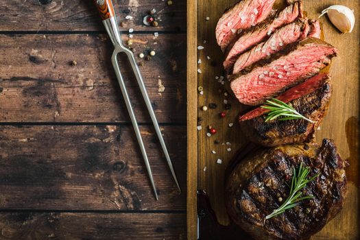 Sliced grilled marbled meat steak Filet Mignon, seasonings, fork, wooden cutting board. Space for text. Juicy meat steak. Beef steak grilled/fried. Top view. Roasted meat steak. Close-up. Rustic