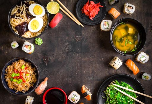 Sushi and japanese food on dark background. Sushi rolls, hiyashi wakame, miso soup, ramen, fried rice with vegetables, nigiri, salmon steak, soy sauce, сhopsticks. Asian/Japanese food frame. Overhead....