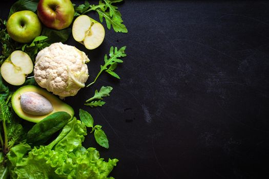 Fresh green vegetables and fruits on black chalk board background. Сauliflower, avocado, spinach, lettuce salad, green apples, herbs. Vegetarian food. Diet/healthy/detox food concept. Space for text