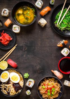 Sushi and japanese food on dark background. Sushi rolls, hiyashi wakame, miso soup, ramen, fried rice with vegetables, nigiri, salmon steak, soy sauce, сhopsticks. Asian/Japanese food frame. Overhead....