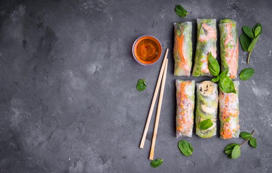 Fresh assorted spring rolls set background. Handmade asian/Chinese spring rolls, sauce, chopsticks. Rustic concrete background. Spring rolls with shrimps, vegetables, fruits. Space for text. Top view