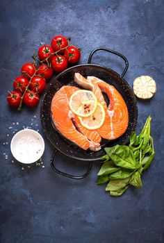 Raw fresh fish with vegetables ready to cook. Raw salmon steaks with lemon, spices and herbs in a pan. Ingredients for cooking on a rustic concrete background. Diet and healthy food. Fish for dinner