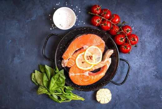 Raw fresh fish with vegetables ready to cook. Raw salmon steaks with lemon, spices and herbs in a pan. Ingredients for cooking on a rustic concrete background. Diet and healthy food. Fish for dinner