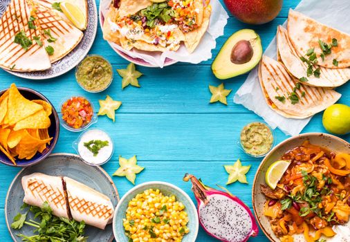Traditional Mexican food background. Table with different Mexican dishes. Cheese nachos, tacos, guacamole, quesadilla, burrito, fajitas, tortilla chips, Mexican fruits. Tex-Mex cuisine. Space for text