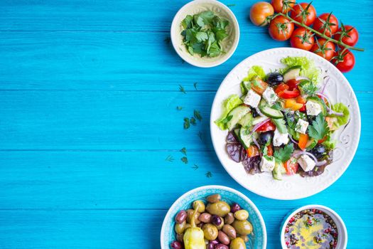 Greek salad background. Bowl with fresh greek salad, tomatoes, olives, olive oil on wooden table. Space for text. Top view. Traditional greek dish. Ingredients for making salad. Mediterranean diet